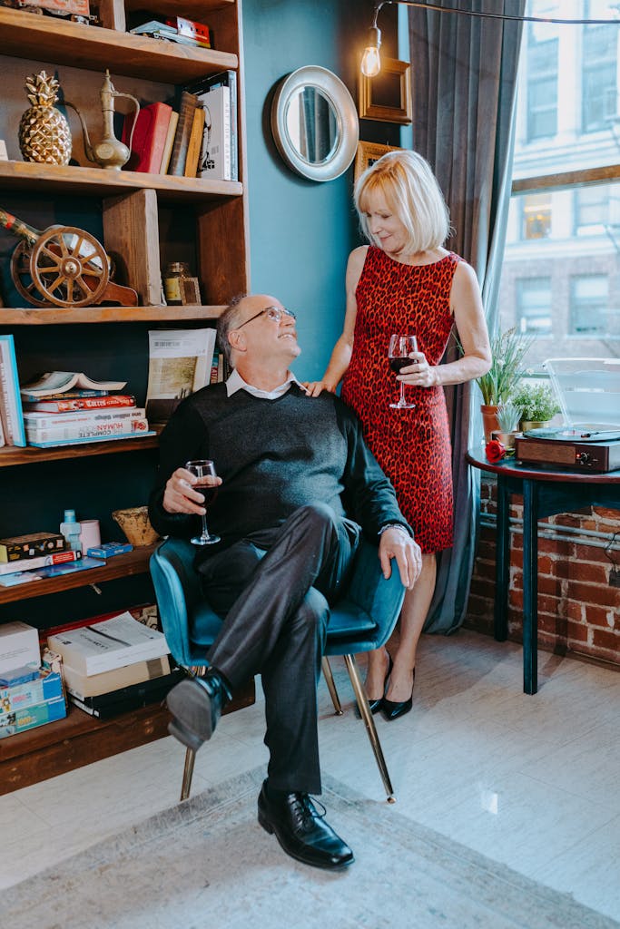 Elderly couple enjoying a glass of wine in a cozy living room setting.