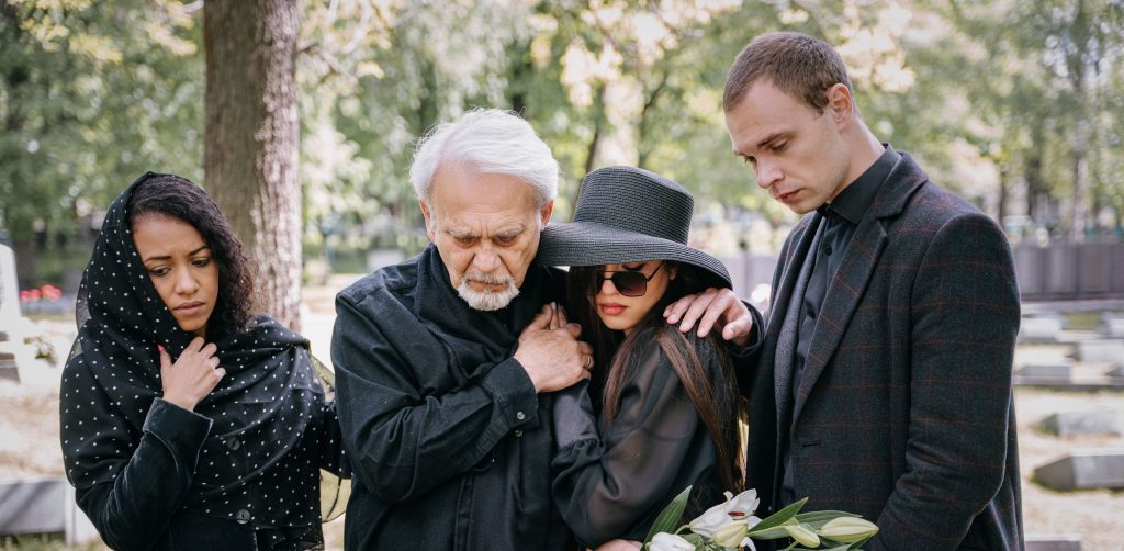 A sorrowful family gathering at a cemetery, embracing and supporting each other.
